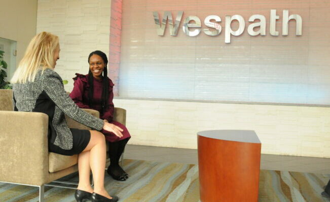 Two woman sitting and talking next to a Wespath sign