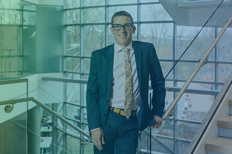 Andy Hendren, CEO, smiling and wearing eyeglasses, a blue suit and yellow tie.