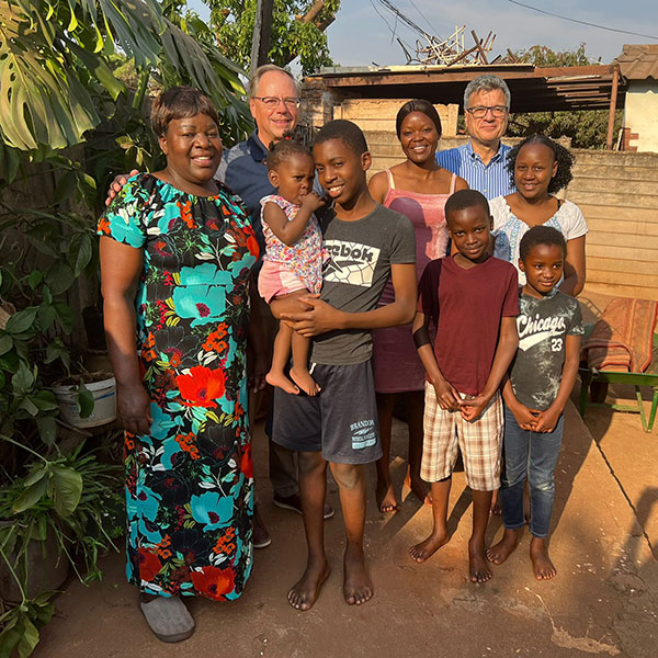 Six adults and three children are standing together outdoors and smiling.