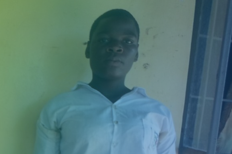 A person in a white shirt stands against a beige wall,