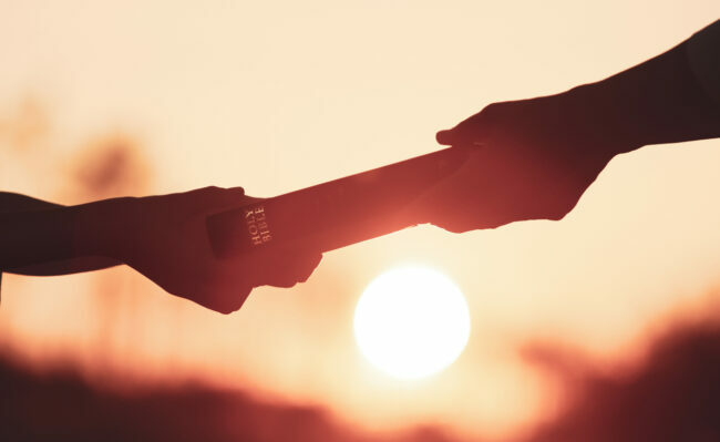 Someone handing another person the bible at sunset