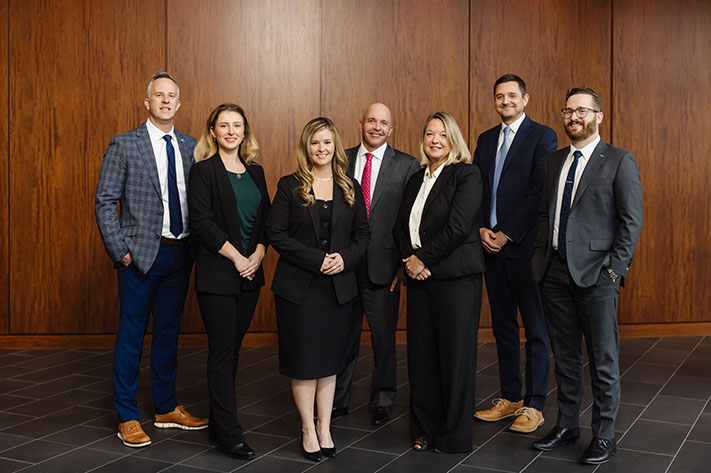 Seven members of the investments team are standing. They are dressed professionally and smiling.