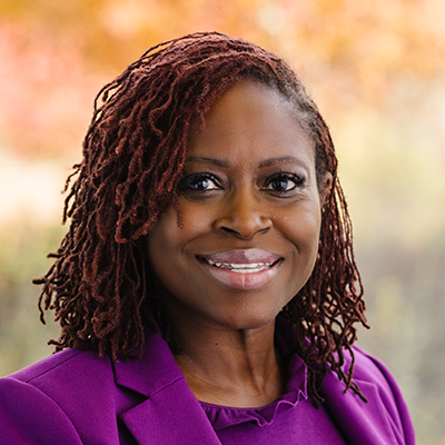 Portrait of Krystal Holmes smiling. She has curly hair and is wearing a purple suit.
