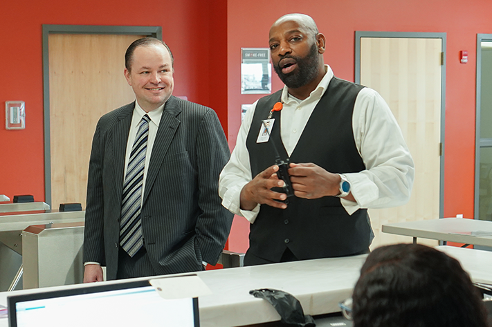 Two men are standing in front of a desk having a discussion.