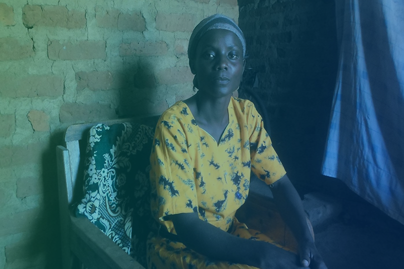 A woman in a yellow patterned dress and headscarf sis sitting on a chair.