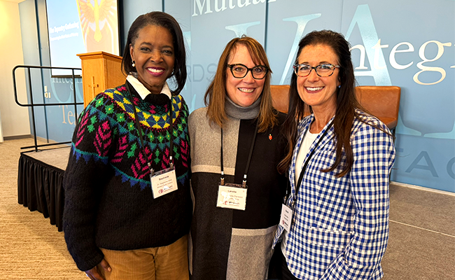 Three women are standing next to each other and smiling.