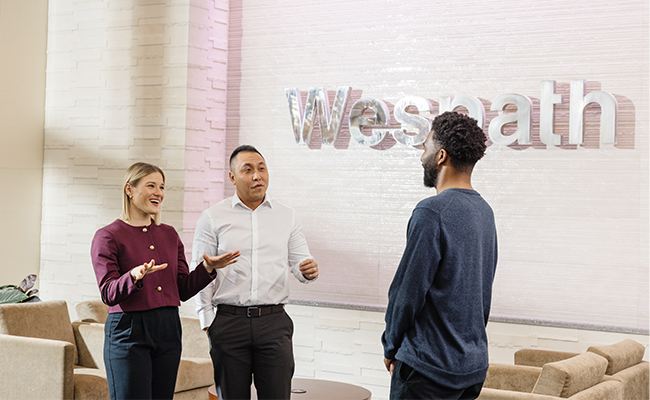 Three Wespath professional team members are having a conversation in front of the Wespath sign.