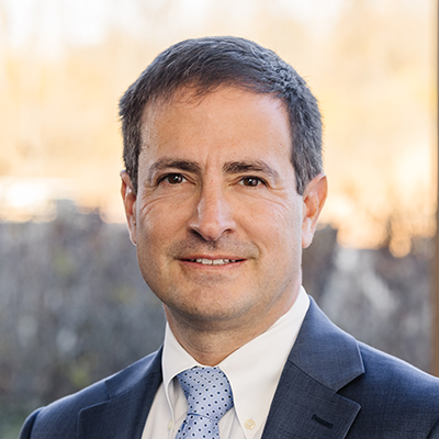 Portrait of Tony Prestipino smiling. He's wearing a navy blazer, white collared shirt and a light blue tie.