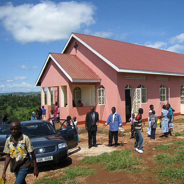 Six people are standing outside of a light red colored church building.